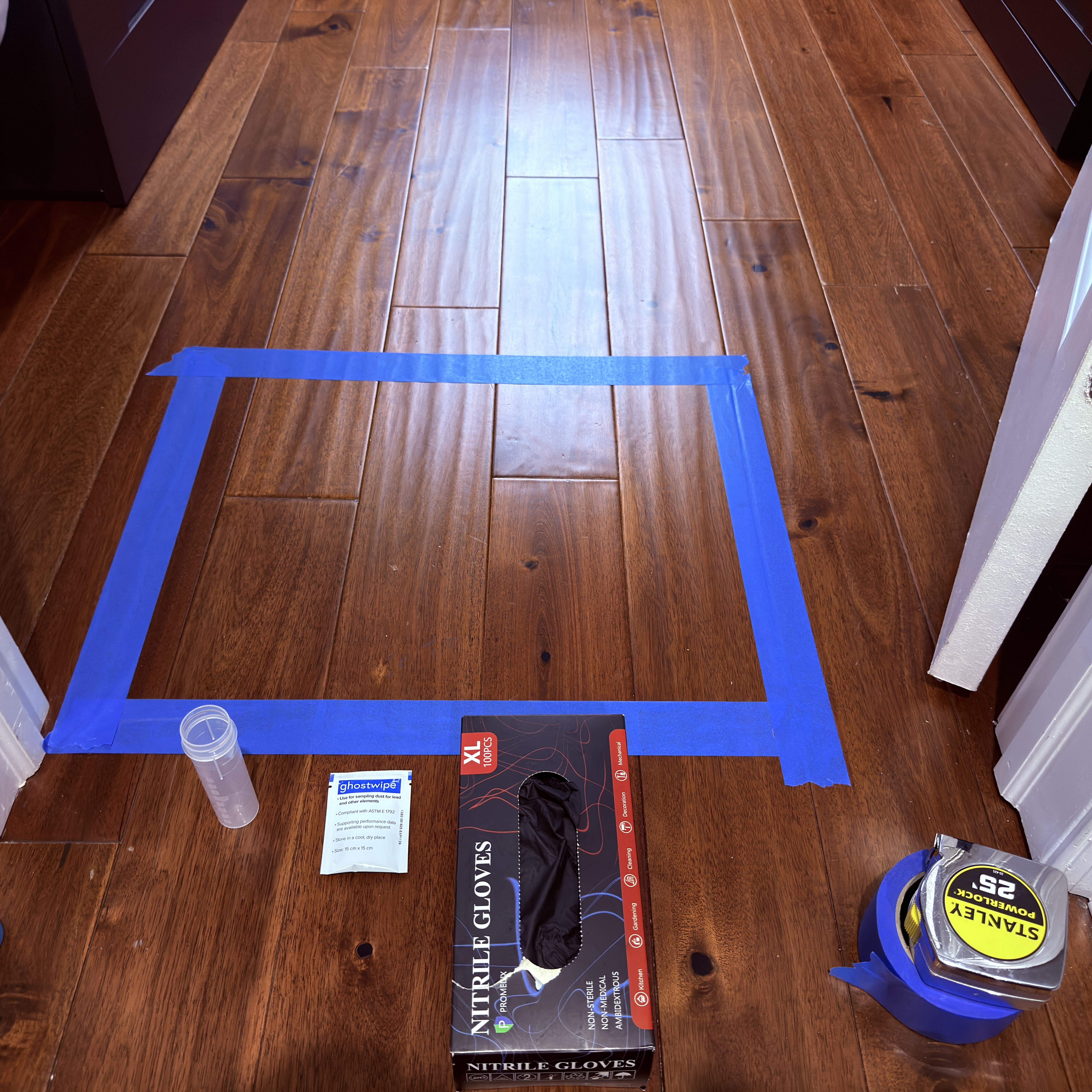 Measured floor sampling area with gloves, dust wipe supplies, and a sample container